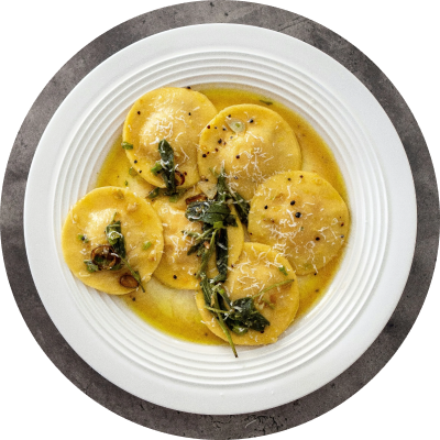 Plated dish of ravioli with a creamy sauce and greens on a white plate.