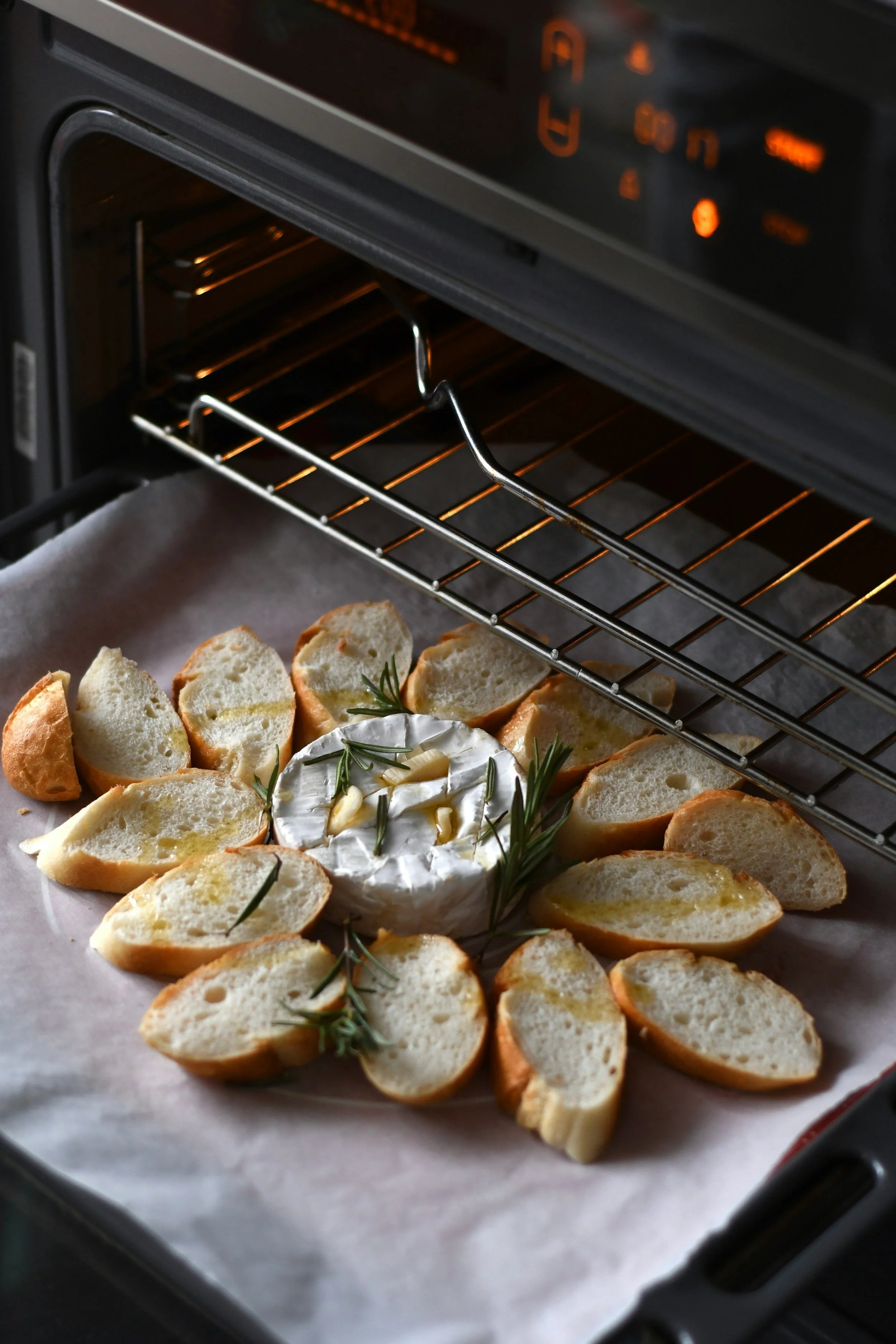 Baked bread slices with a dish of cream cheese and rosemary in an oven.