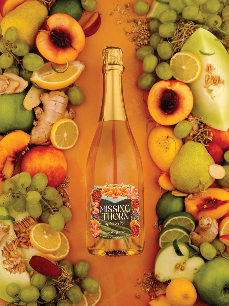 Bottle of Missing Thorn sparkling wine surrounded by fruits on a vibrant background