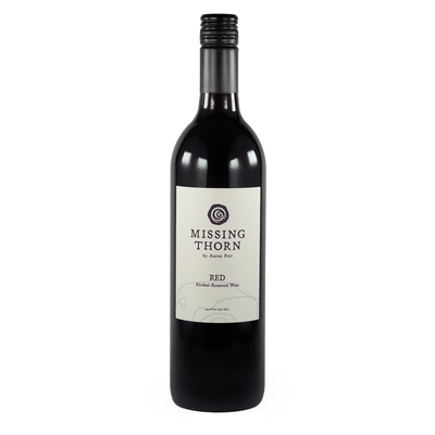 A bottle of non-alcoholic red wine labeled 'Missing Thorn' with a deep purple hue and a bright magenta rim.