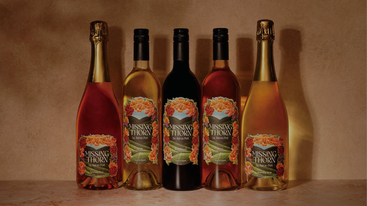 Five bottles of Missing Thorn wine on a wooden surface with a brown background